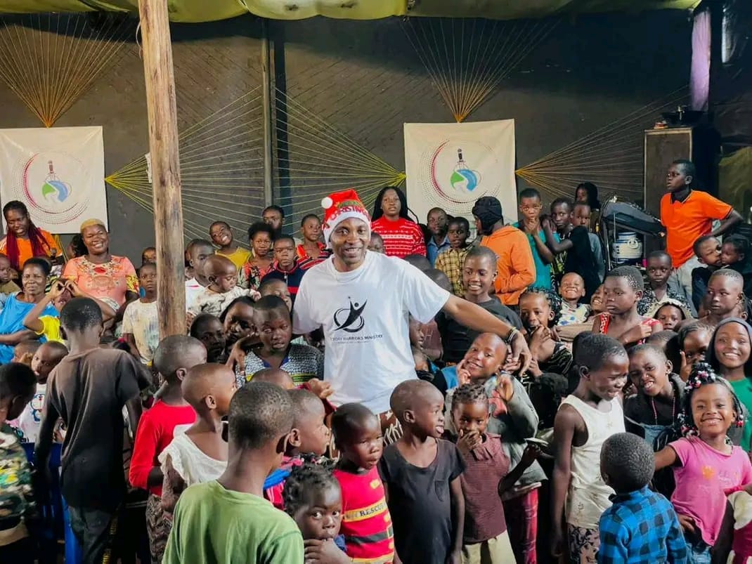 A volunteer in a Santa hat standing with a large crowd of children at the Christmas celebration